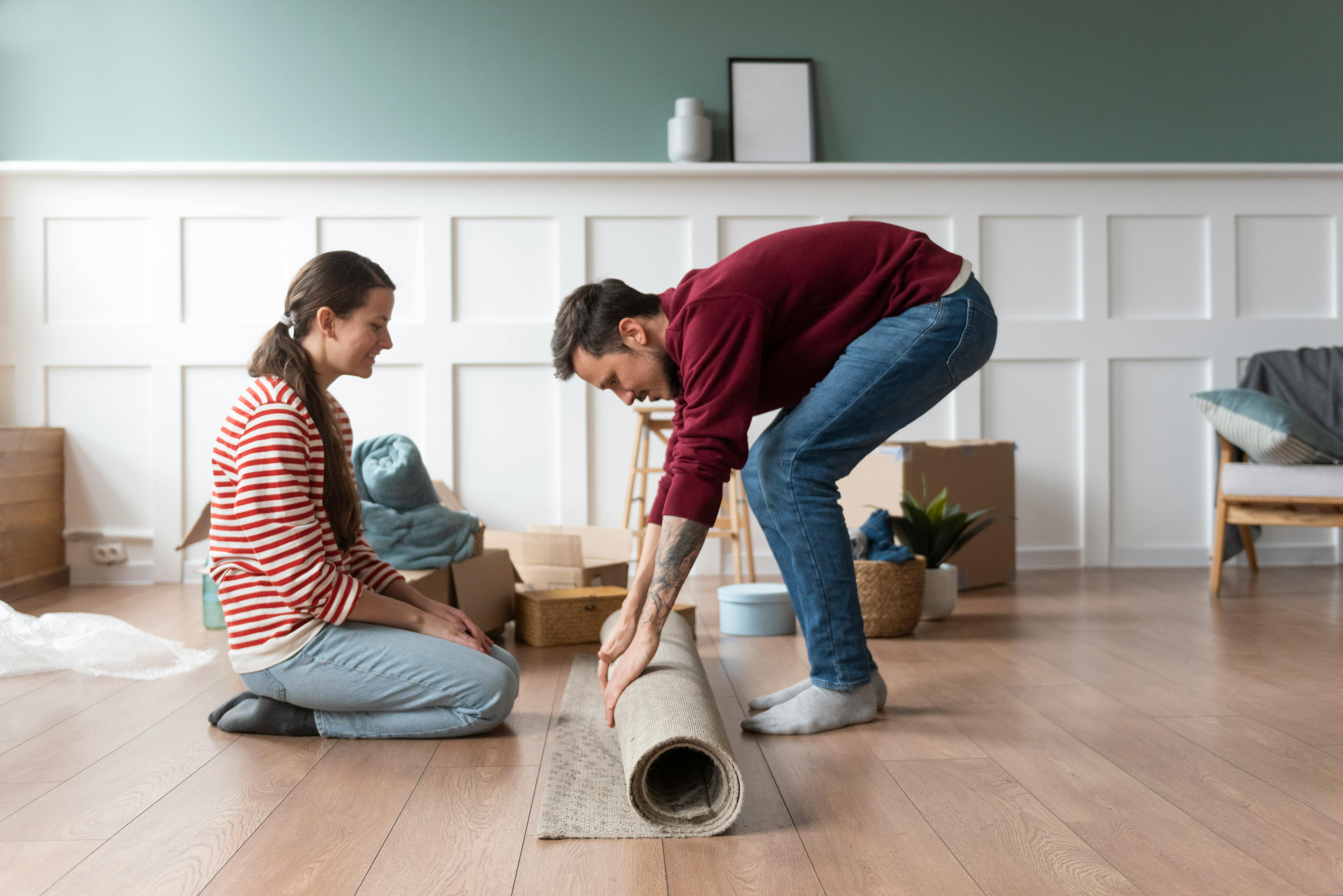 Junges Paar legt ein Teppich &uuml;ber ihren ged&auml;mmten Laminatboden von LaminatDEPOT