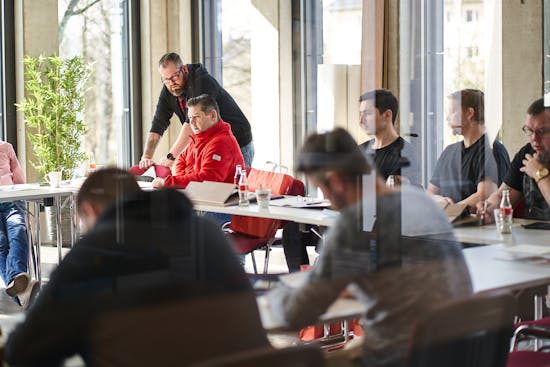 Mehrere Menschen sitzen bei Schulung am Tisch und hören zu